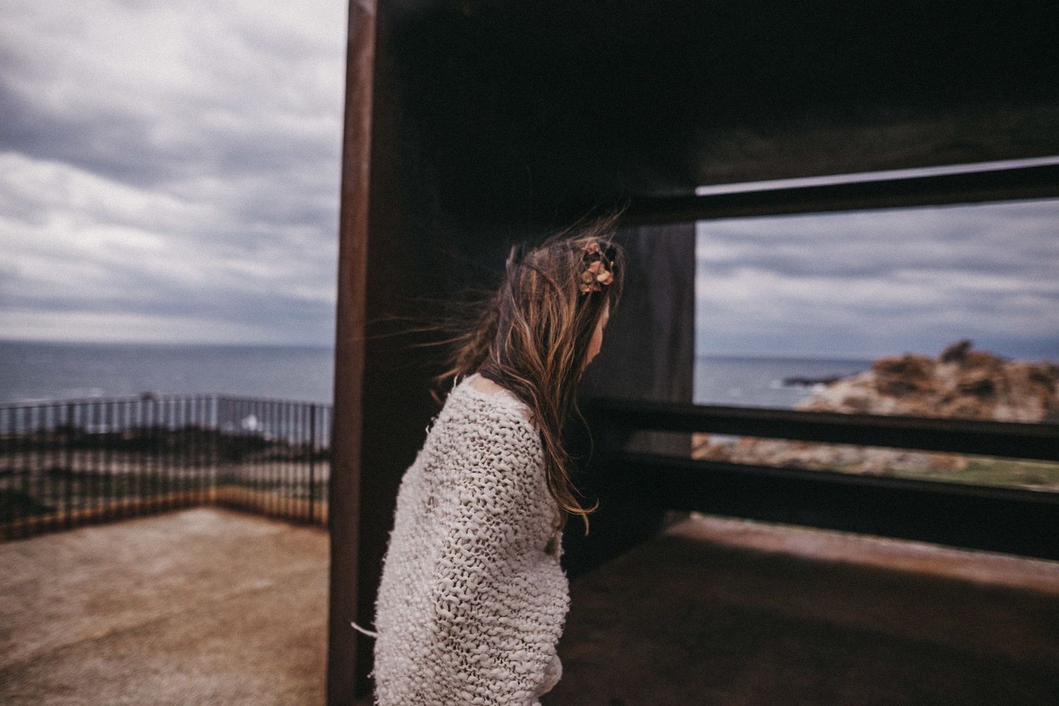 A person in white gazes out from a modern viewing structure overlooking a coastal landscape.