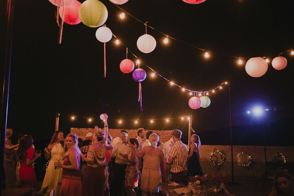Crowd dances beneath colorful paper lanterns and string lights at outdoor night celebration.