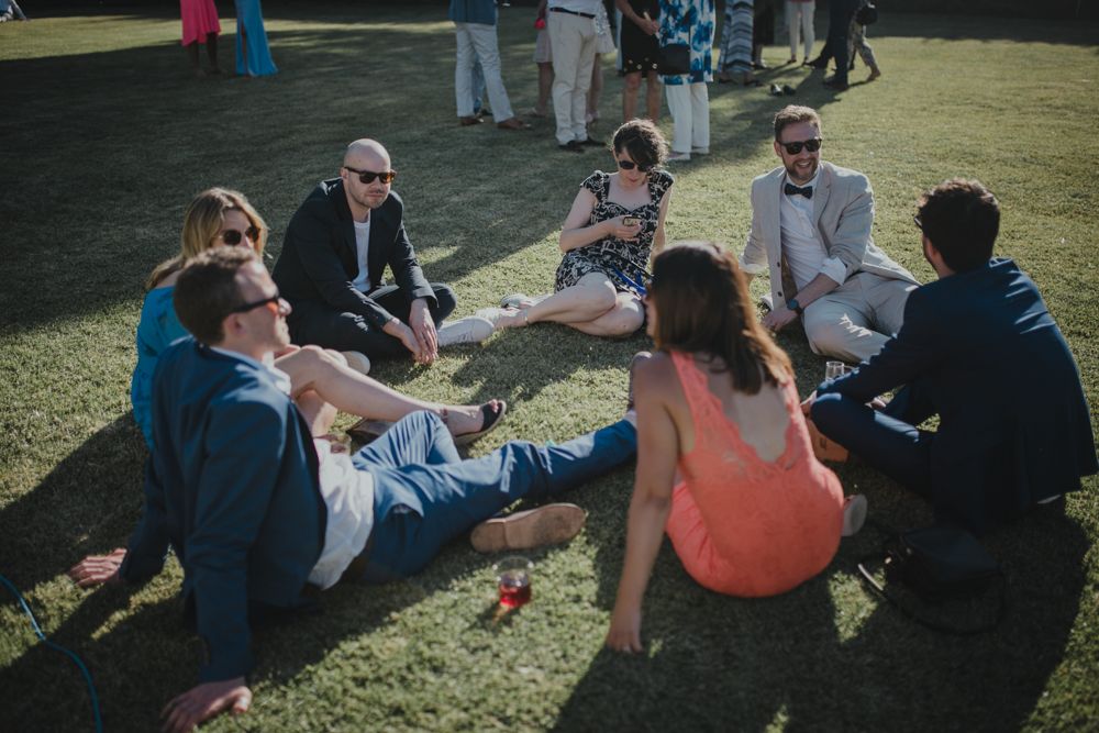 Wedding guests lounging in casual circle on lawn during outdoor reception.