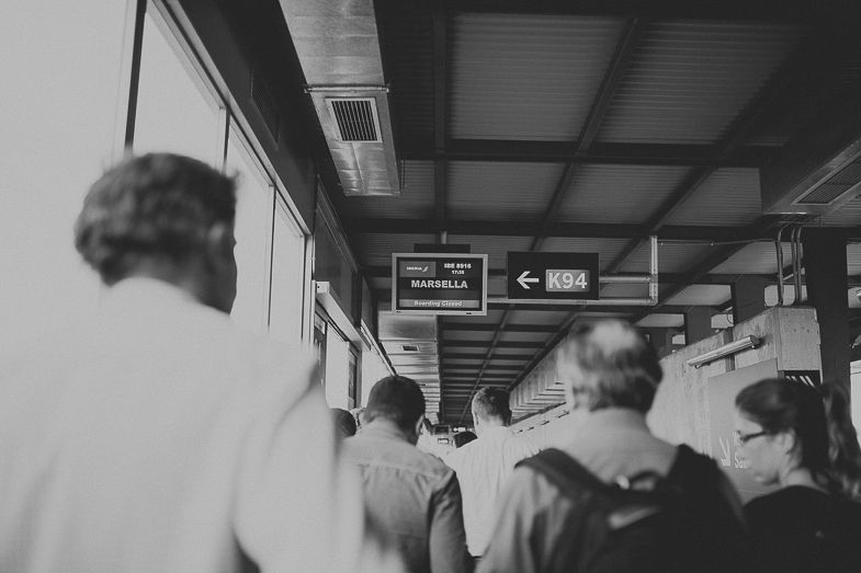 Passengers walking through an airport terminal hallway in black and white.