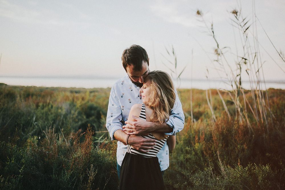 Intimate embrace between two people in a field during sunset.