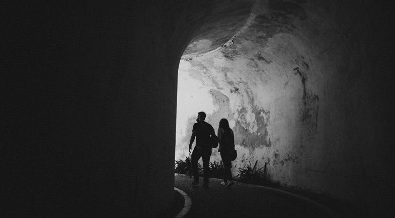 Silhouetted figures walking through a dark tunnel with bright light at the end.