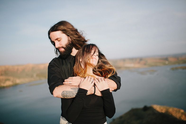Intimate couple embracing against a scenic waterfront landscape.