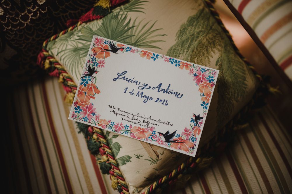 A floral-bordered wedding invitation card displayed on a patterned fabric.