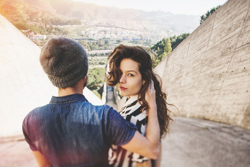 Couple against concrete walls with cityscape and mountains visible in background.