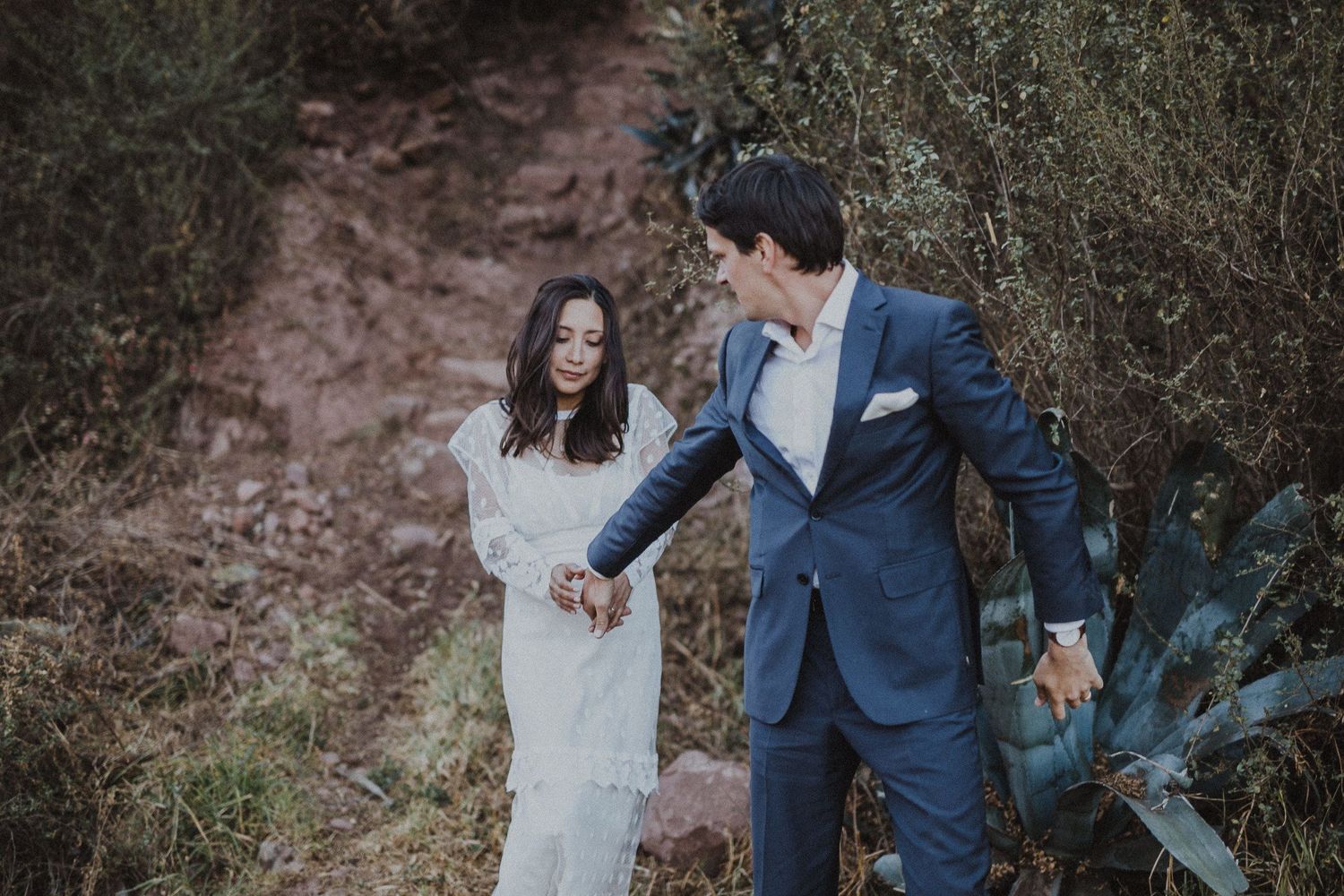 A couple in wedding attire shares a playful moment on a rustic path.