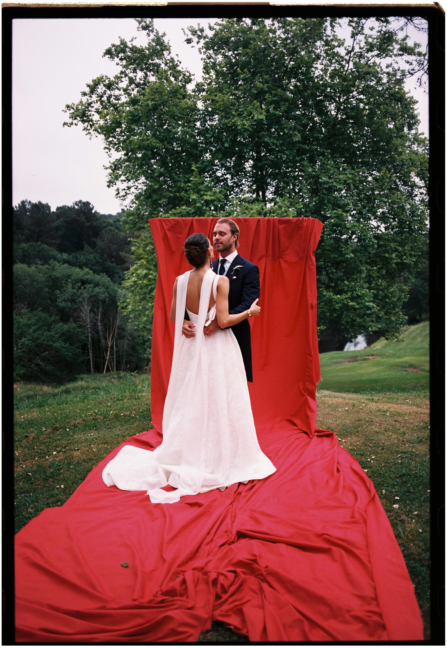 A couple poses against a dramatic red fabric backdrop outdoors during their wedding photoshoot.