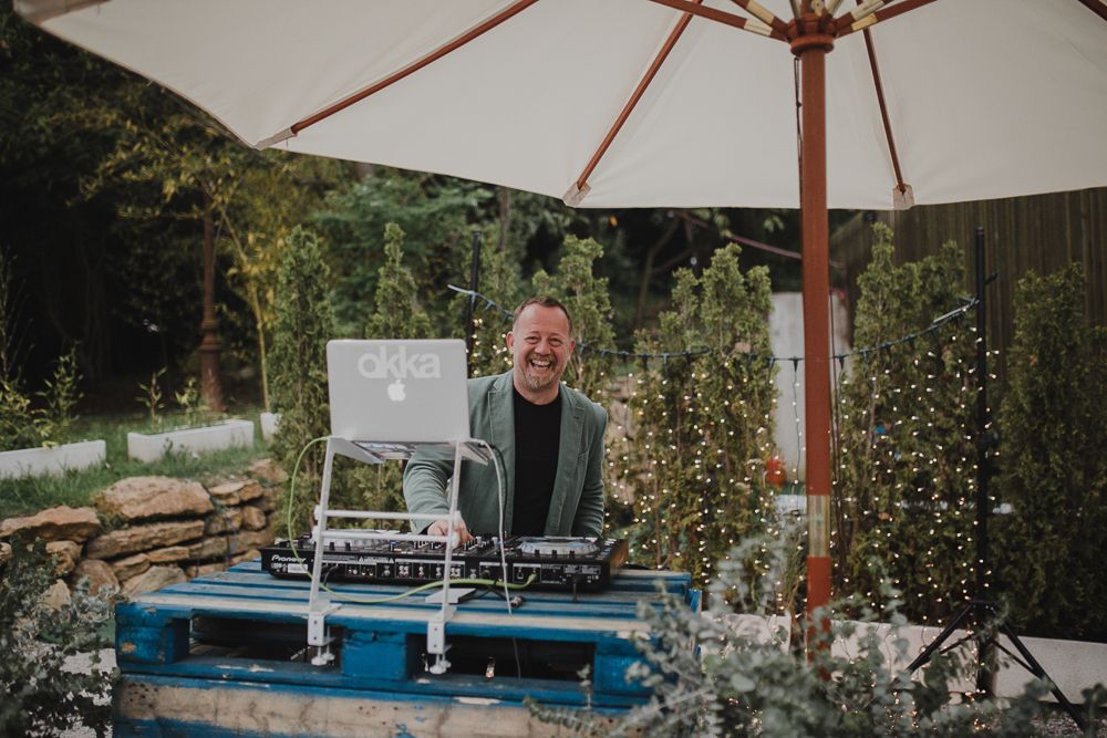 DJ performs at an outdoor wedding reception under a white market umbrella.
