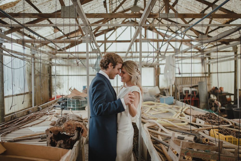 Wedding couple embracing in an industrial warehouse with exposed wooden beams and natural light.