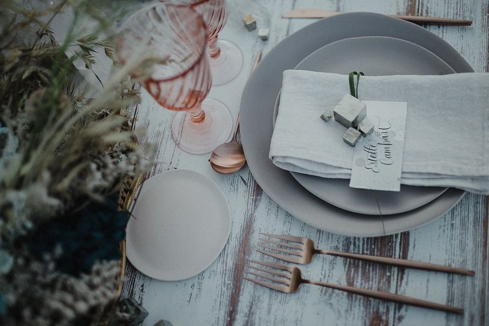 Elegant place setting with gray plates, linen napkin, and vintage tag on distressed wood table.