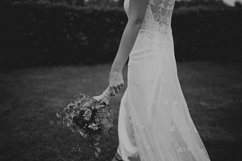 Black and white photo of a bride holding a floral bouquet in her lace wedding gown.