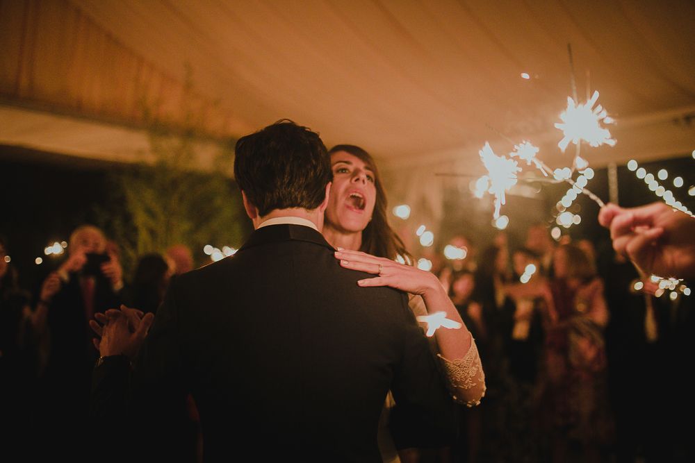 Couple dancing at a wedding reception with sparklers and guests celebrating in the background.