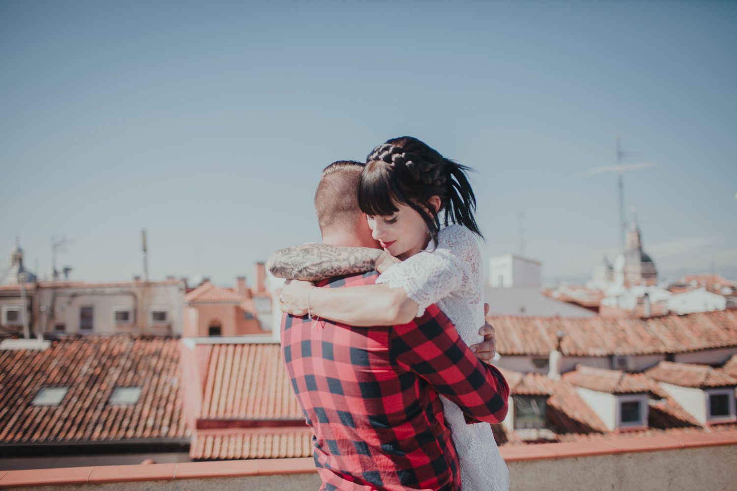A couple sharing an intimate moment on a rooftop with Spanish-style buildings in the distance.
