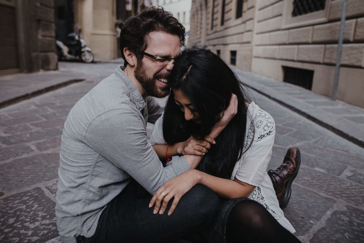 A joyful couple sharing laughter while sitting together on a cobblestone street.