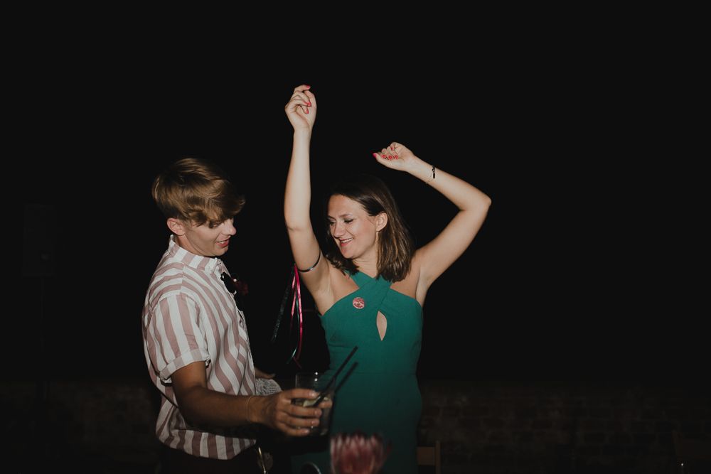 Two people dance energetically at a nighttime party with drinks in hand.