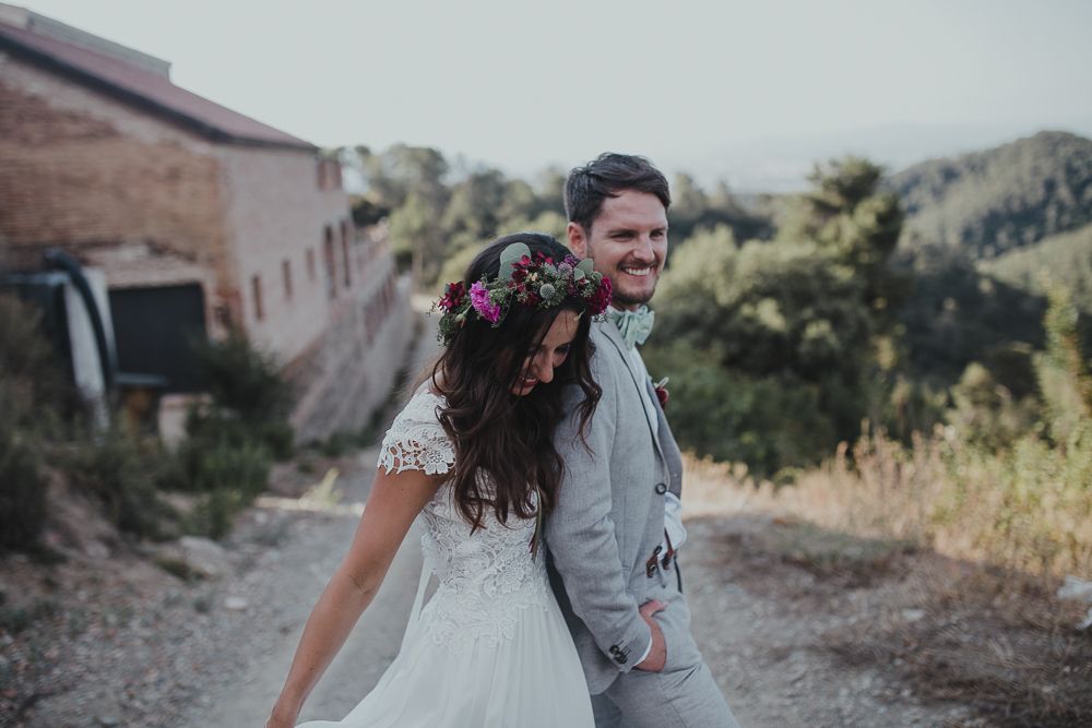 Candid wedding moment captured on mountain path with rustic building in background.