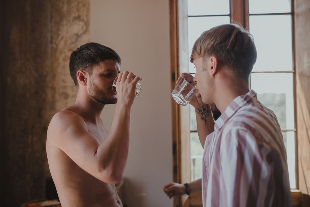 Two people drinking from glasses near a window in casual morning light.
