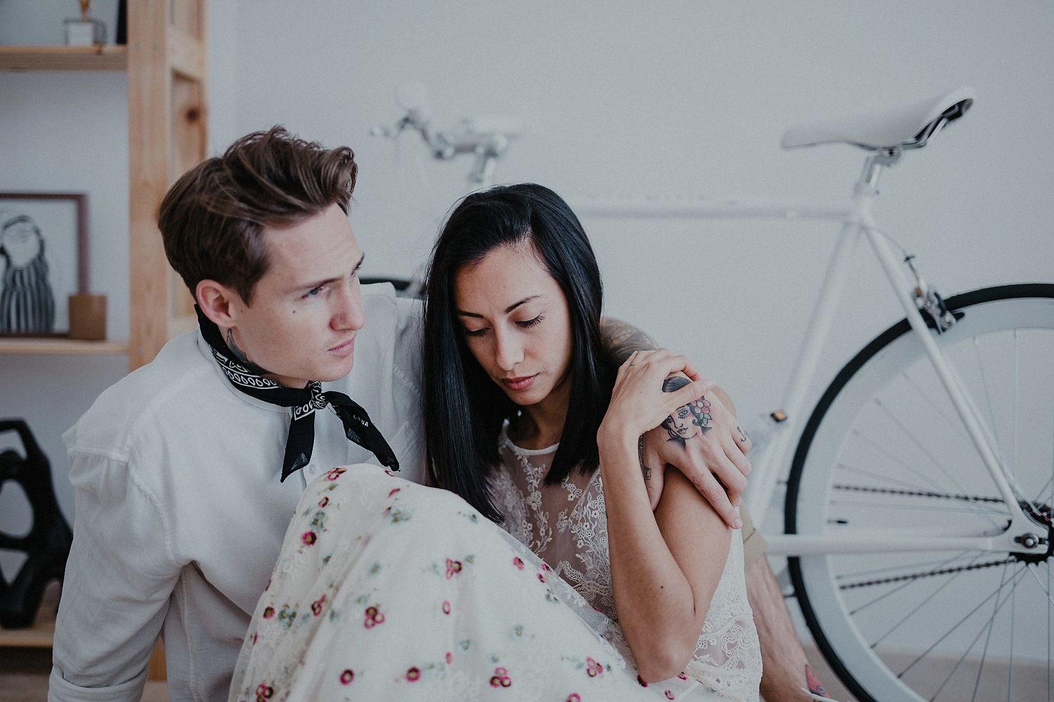 Tender moment captured indoors with vintage bicycle and wooden shelving in background.