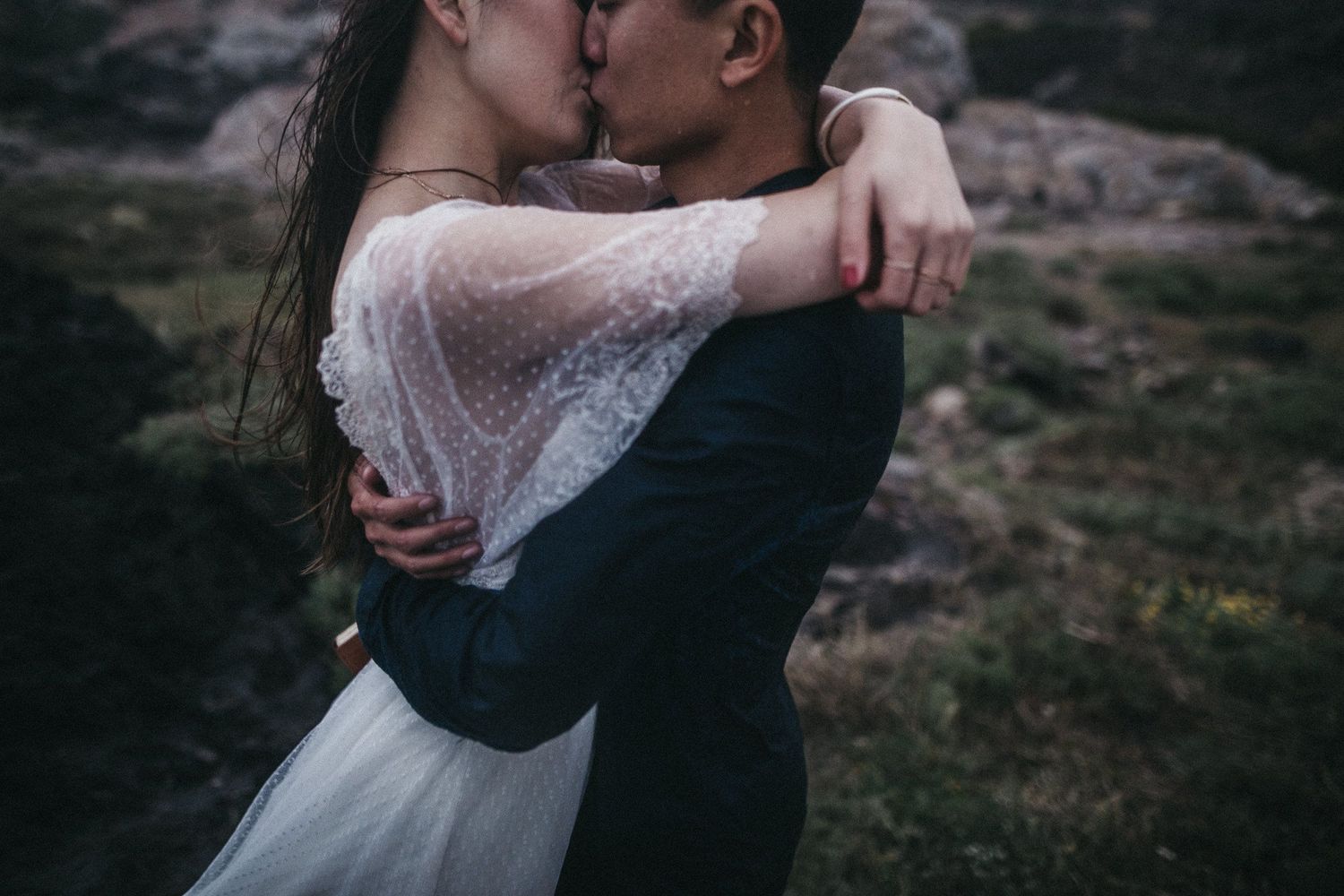 A couple in wedding attire shares an intimate kiss in nature.