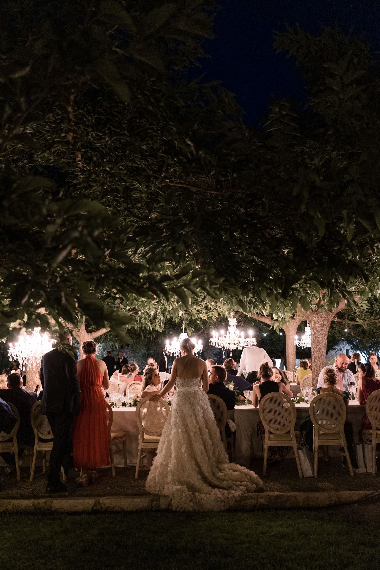 Romantic outdoor wedding reception under illuminated trees at night with elegantly set dining tables.