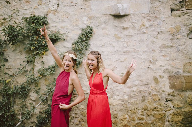 Two women in red dresses posing joyfully against a stone wall.