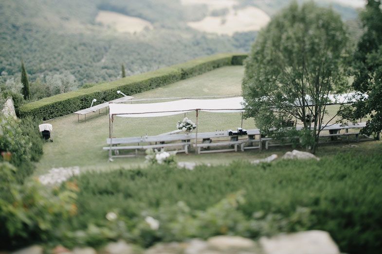 Outdoor benches and tables set against a hillside landscape with trees and mountains in the background.