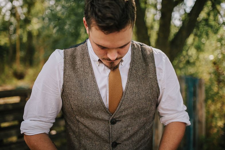 Person wearing brown vest and white shirt adjusts clothing outdoors.