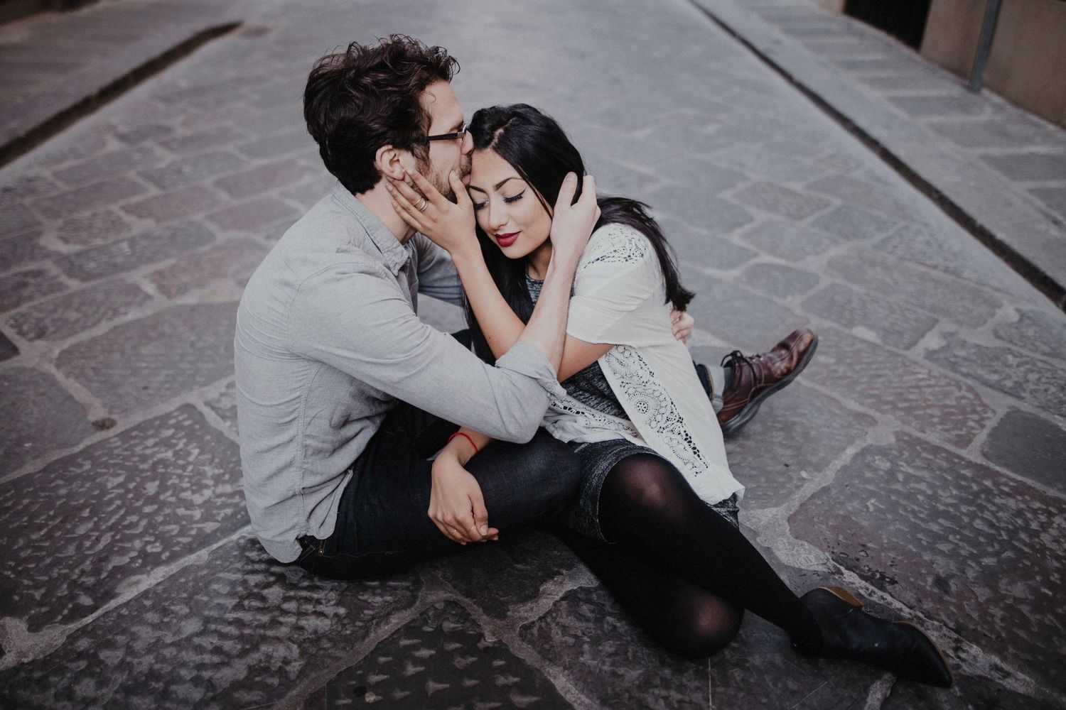 A romantic couple sitting close together on stone pavement sharing an intimate moment.