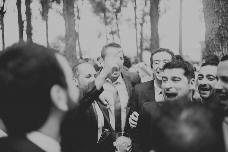 A black and white photo captures groomsmen laughing and celebrating at a wedding.