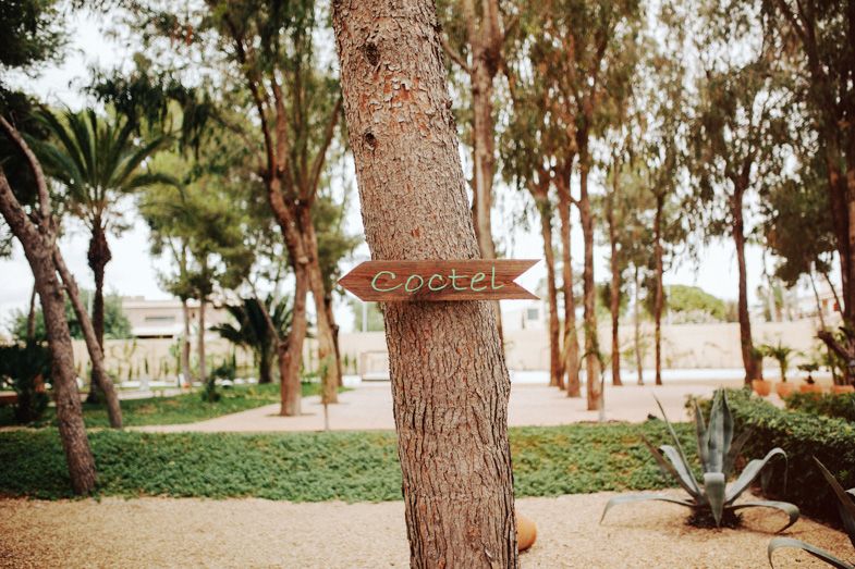 Wooden directional sign attached to a tree trunk in an outdoor wedding venue.