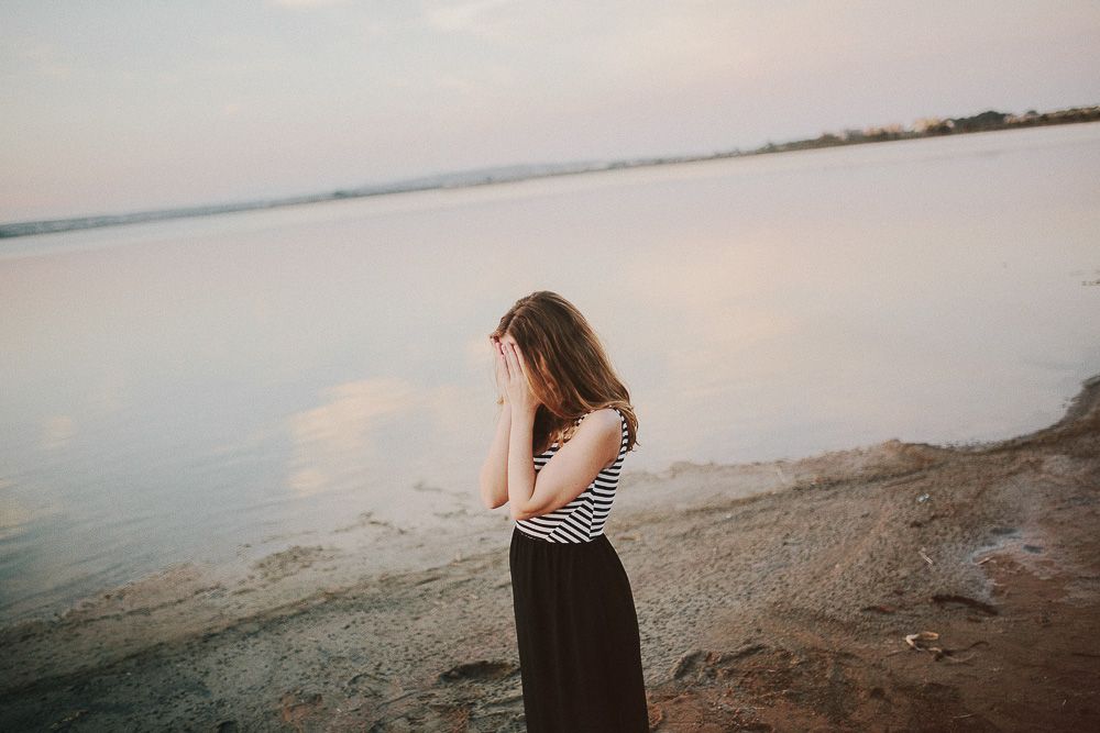 Person in striped top standing alone by peaceful lake at dusk.