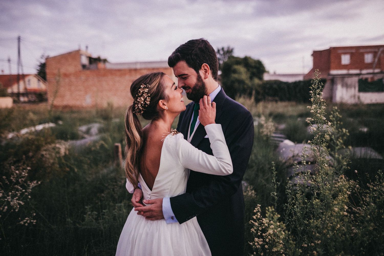 A romantic wedding photo captured in a field at dusk with blooming wildflowers in the background.