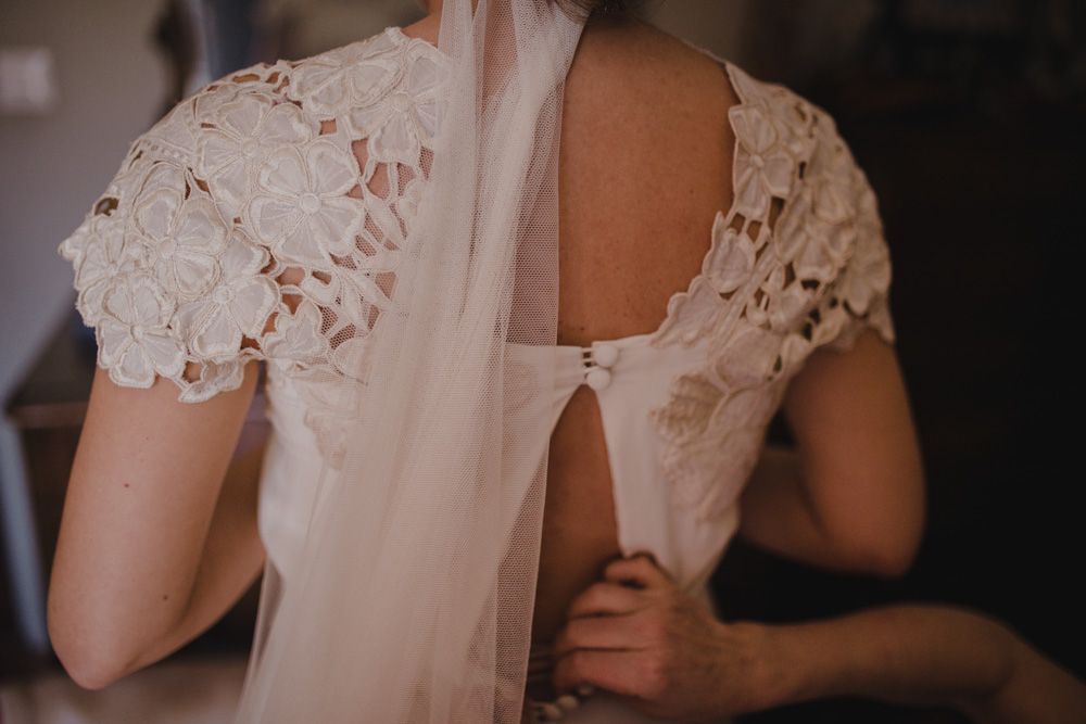 Close-up detail of delicate white lace on a wedding dress with button closure.