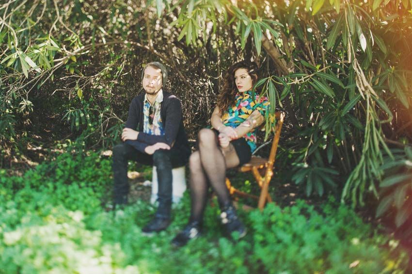 Two people sitting in a lush garden setting with greenery and natural lighting.