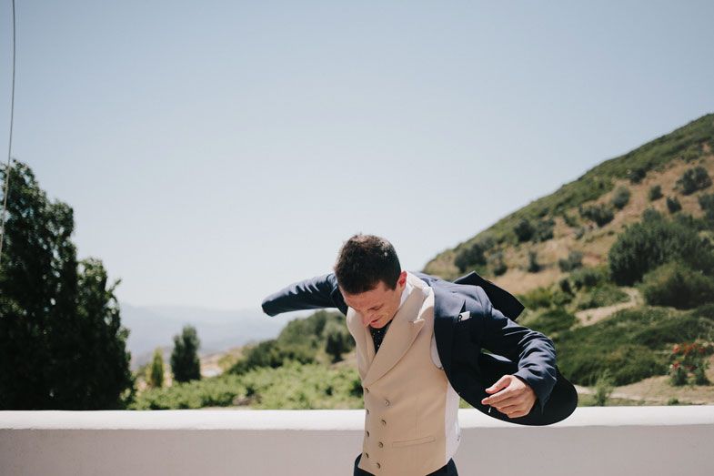 Person in a tan vest and backpack walking on a path with scenic mountain views in the background.