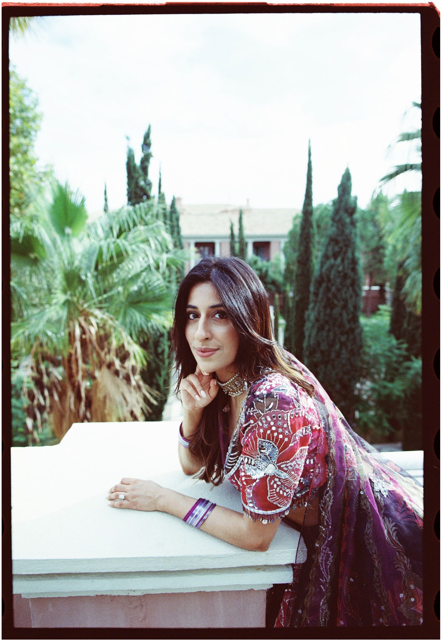 Film portrait of Elina leaning on the terrace balustrade in a purple outfit.