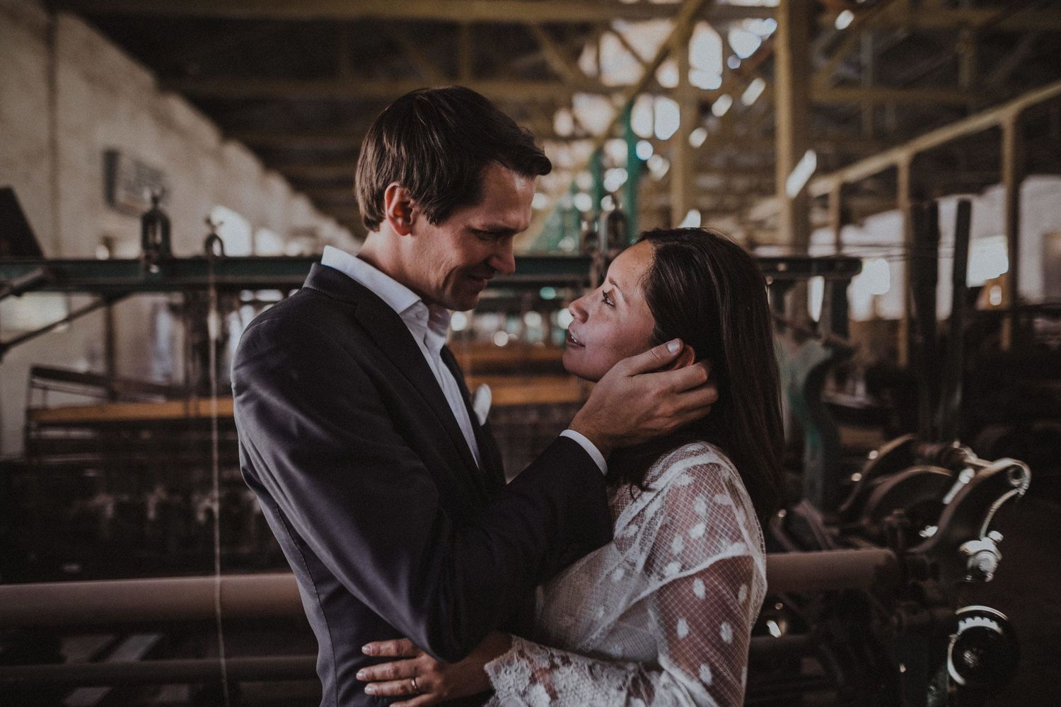 Tender moment between newlyweds in an atmospheric industrial warehouse with vintage machinery.