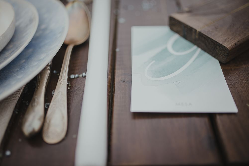 Minimalist table setting detail with white plates and silverware on dark wood.