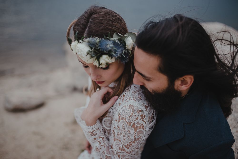 A romantic lakeside portrait featuring intricate lace and floral crown details.