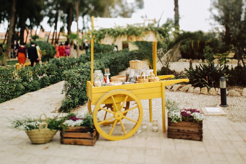 A charming yellow vintage cart decorated with flowers and wooden crates in an outdoor garden setting.