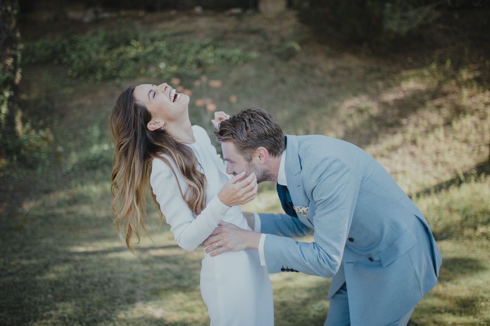 Joyful wedding couple sharing a playful moment outdoors in formal attire.