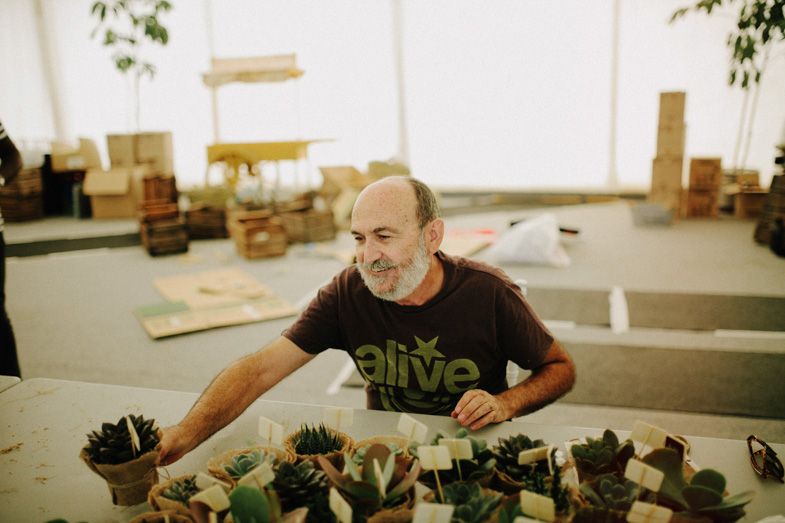 Worker arranging succulent plants on a wooden table in workshop setting.