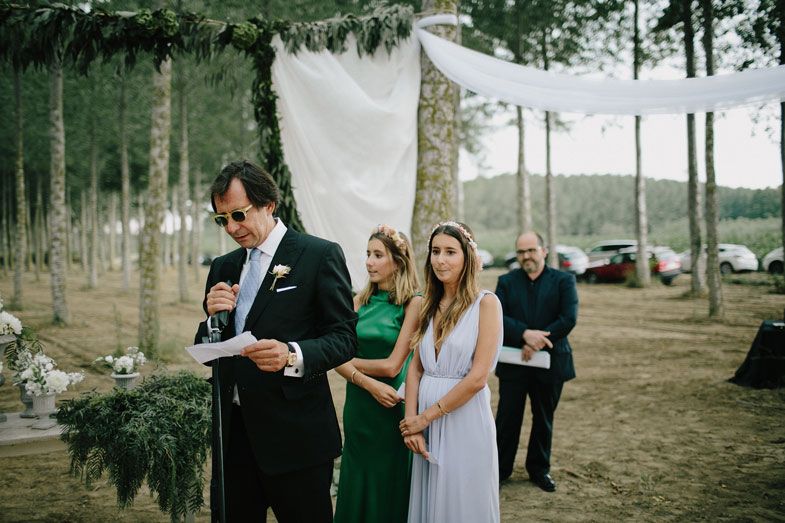 Wedding ceremony in progress with decorative greenery and white fabric in forest setting.