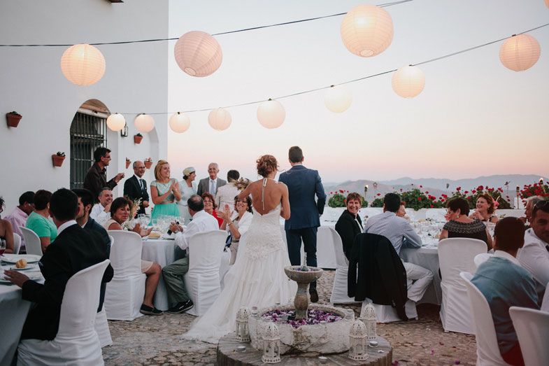 Wedding guests enjoying dinner under strings of glowing paper lanterns at dusk.