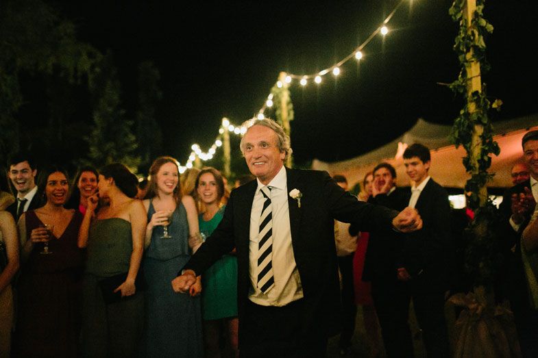 Party guests dancing and celebrating under string lights at an outdoor evening celebration.