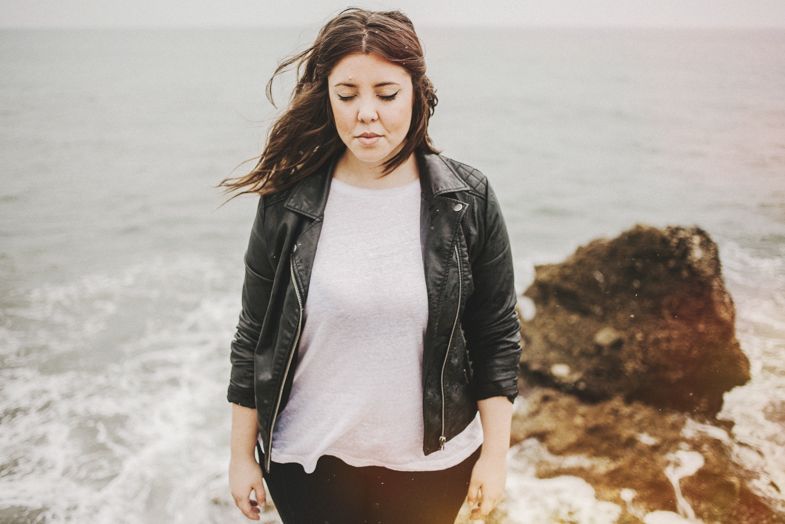 A figure in a black leather jacket stands against a dramatic rocky coastline.