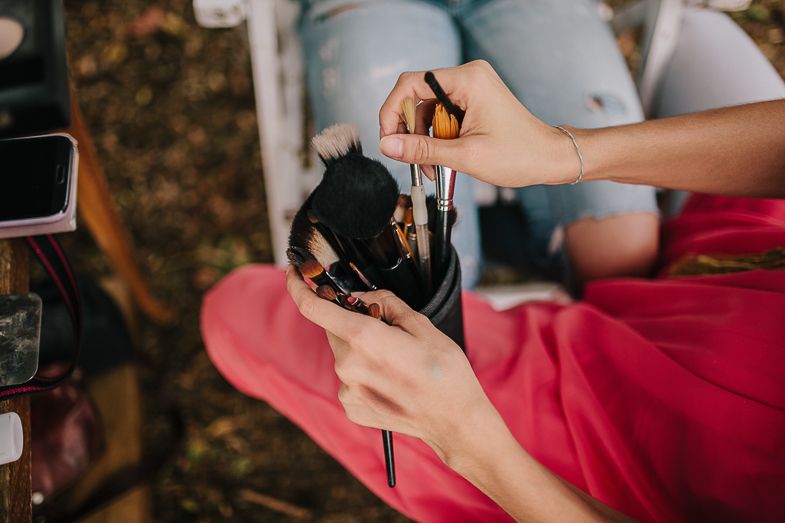 Close-up of hands organizing makeup brushes and tools during an outdoor photo session.