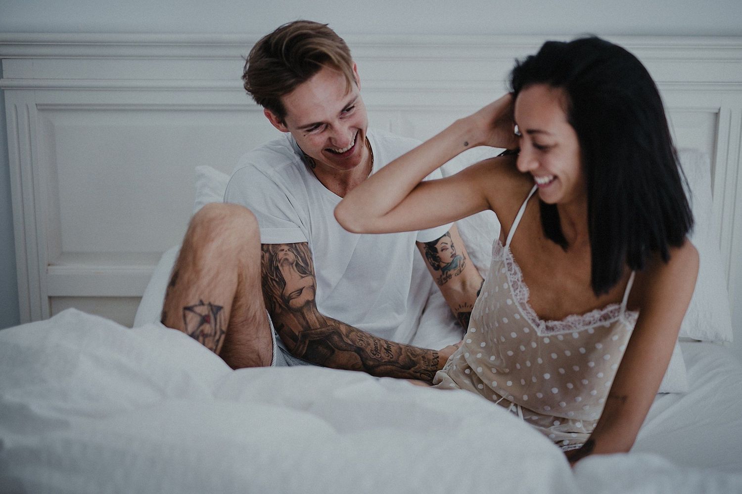 Couple laughing together while relaxing on white bedding.