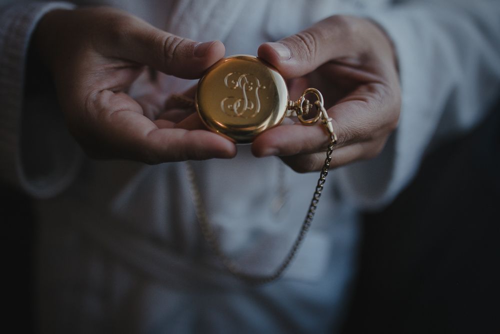 Hands holding an antique gold pocket watch with monogram detail.