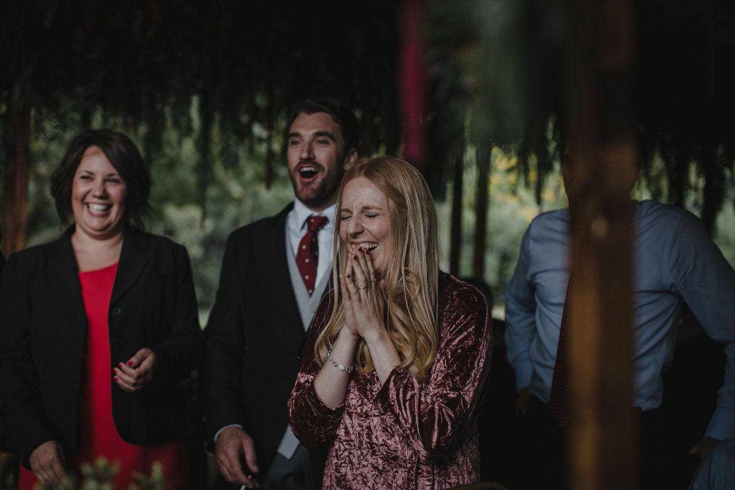 A group enjoying a lighthearted moment at an outdoor celebration with natural lighting and foliage in the background.